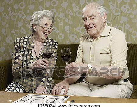 Picture - Senior couple drinking red wine make a toast on the couch. Fotosearch