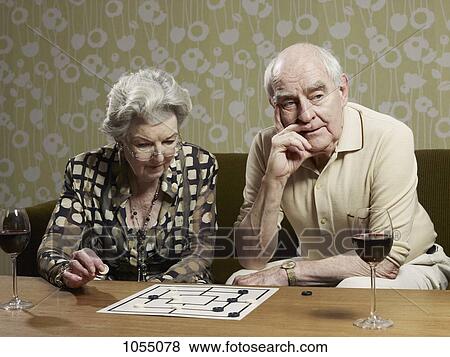 Stock Photo - Senior couple play muehle and man looks impatient. Fotosearch