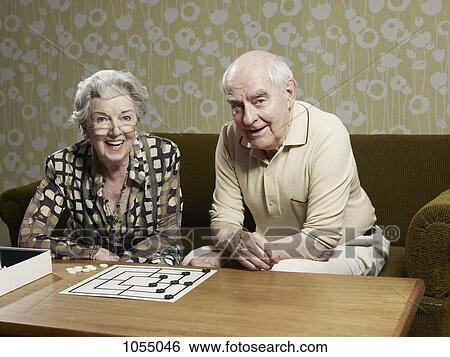 Stock Photograph - Senior man and woman play muehle on couch. Fotosearch