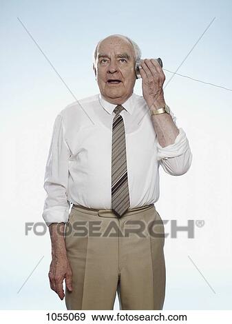 Senior man comically strains to hear on a tin can phone View Large Photo Image Stock Photo - Senior man comically strains to hear on a tin can phone. Fotosearch