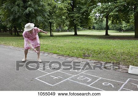 Stock Photo - Senior woman rolls a stone as she plays hopscotch. Fotosearch