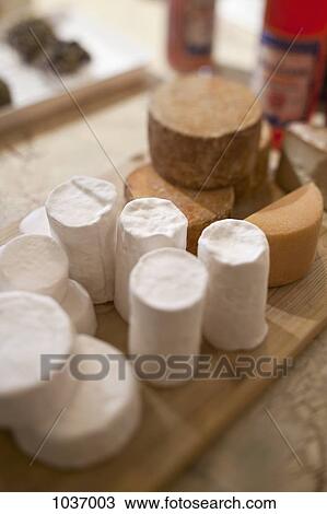 Stock Image - Several kinds of wrapped cheeses on wooden chopping board on table. Fotosearch