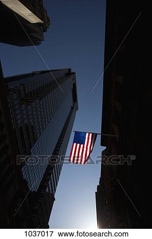 The American flag shown between skyscrapers with a backdrop of a clear blue sky View Large Photo Image Stock Photo - The American flag shown between skyscrapers with a backdrop of a clear blue sky. Fotosearch