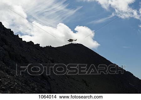 Picture - The Wetterstein, Tirol, Austria, Helicopter in distance above a silhouetted mountain. Fotosearch