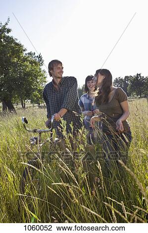 Three friends amongst the timothy grass walk with bike View Large Photo Image Stock Image - Three friends amongst the timothy grass walk with bike. Fotosearch