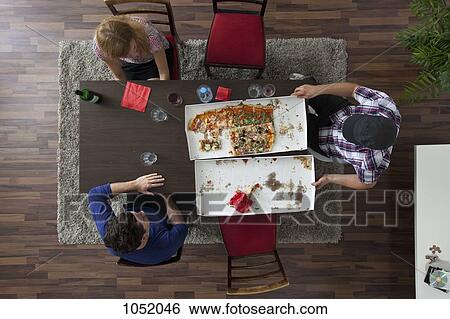 Three friends relaxing around a table after eating pizza, overhead view View Large Photo Image Stock Photograph - Three friends relaxing around a table after eating pizza, overhead view. Fotosearch