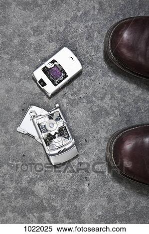 Stock Photography - Two booted feet next to a smashed mobile phone. Fotosearch