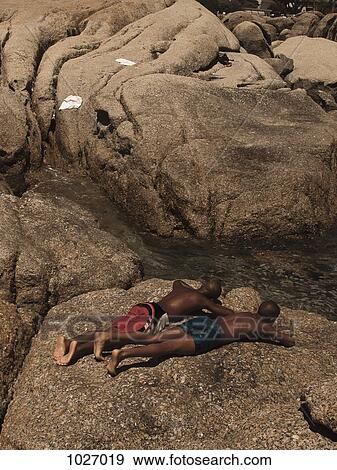 Two men sunbathing on a large rock by a stream View Large Photo Image Stock Photo - Two men sunbathing on a large rock by a stream. Fotosearch