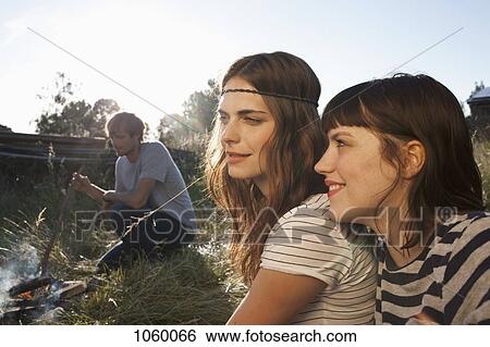 Two smiling girls in foreground with guy in background poking fire in field View Large Photo Image Stock Photograph - Two smiling girls in foreground with guy in background poking fire in field. Fotosearch