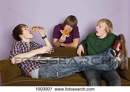 Stock Photo - Two teenage boys eating pizza while another watches enviously. Fotosearch