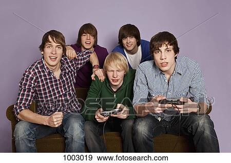 Two teenage boys playing a video game while their friends cheer them on View Large Photo Image Stock Photo - Two teenage boys playing a video game while their friends cheer them on. Fotosearch