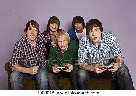 Stock Photography - Two teenage boys playing a video game while their friends cheer them on. Fotosearch