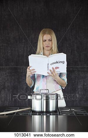 Stock Image - Woman cooking confused by cookery book.. Fotosearch