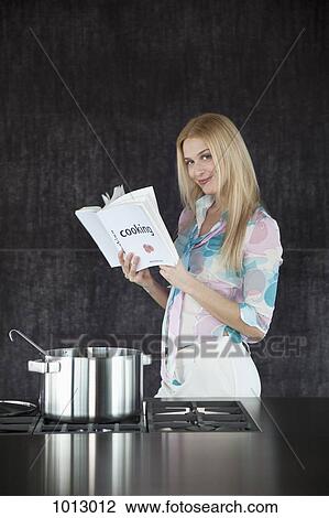 Woman cooking, content holding a cookery book. View Large Photo Image Stock Image - Woman cooking, content holding a cookery book.. Fotosearch