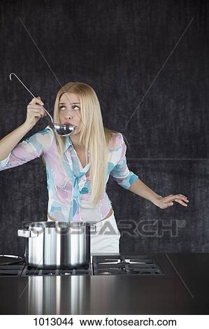Woman cooking, tasting from a ladle and looking up. View Large Photo Image Picture - Woman cooking, tasting from a ladle and looking up.. Fotosearch