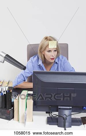 Stock Photography - Woman looking at computer with adhesive note stuck on her forehead. Fotosearch