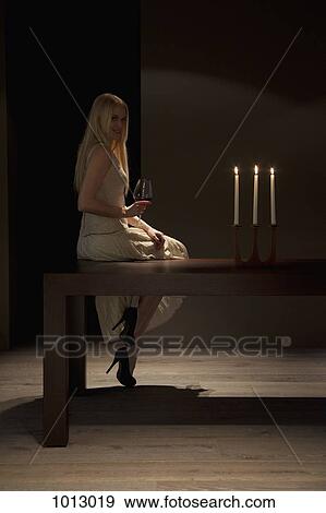 Stock Photo - Woman sits on table with red wine by candlelight.. Fotosearch
