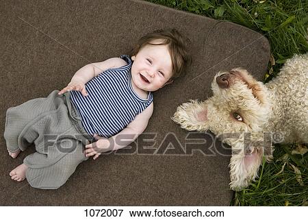 Stock Photo - A baby girl and dog lying outside. Fotosearch