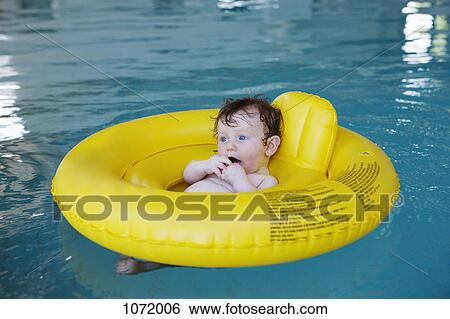 Stock Photograph - A baby girl floating in an inflatable ring at an indoor pool. Fotosearch