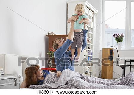 Stock Photo - A couple in bed, man holding daughter aloft. Fotosearch