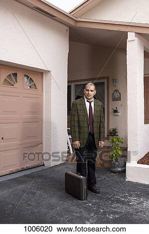 Stock Image - A defeated looking businessman standing in his driveway. Fotosearch