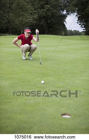 Stock Photograph - A female golfer crouching down studying the distance to the hole. Fotosearch