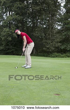 Stock Image - A female golfer preparing to putt . Fotosearch