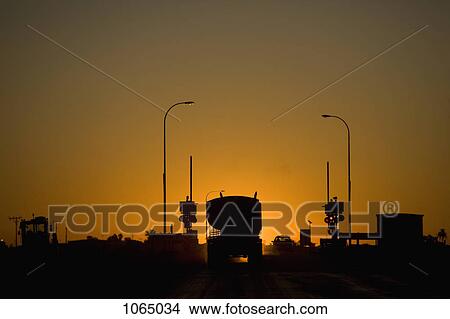 A freight truck and car stopped at a railroad crossing silhouetted against the setting sun View Large Photo Image Picture - A freight truck and car stopped at a railroad crossing silhouetted against the setting sun. Fotosearch
