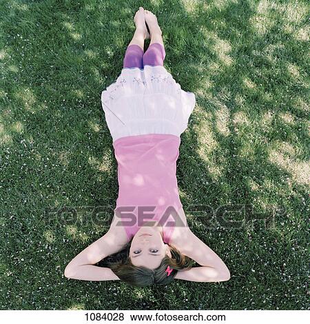 Stock Photo - A girl lying in grass with hands behind head, upside down view. Fotosearch