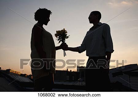 A man giving flowers to a woman on a rooftop terrace at sunset View Large Photo Image Stock Image - A man giving flowers to a woman on a rooftop terrace at sunset. Fotosearch