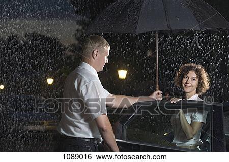 Stock Photograph - A man opening a car door and holding an umbrella over a woman. Fotosearch