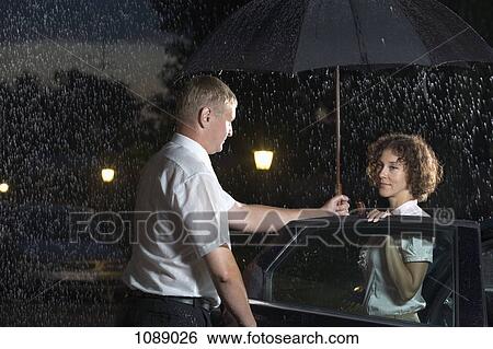 A man opening a car door and holding an umbrella over a woman View Large Photo Image Stock Photograph - A man opening a car door and holding an umbrella over a woman. Fotosearch