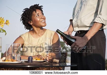 Stock Image - A man pouring champagne for a woman on a rooftop terrace. Fotosearch