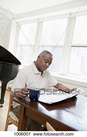 Stock Photo - A mature man sitting at a dining table reading a newspaper. Fotosearch