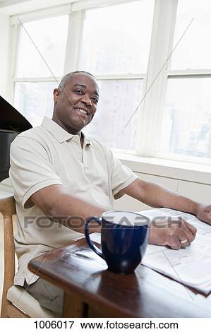 Stock Photo - A mature man sitting at a dining table with coffee mug and newspaper. Fotosearch