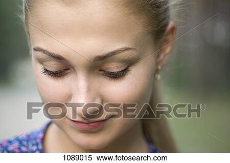 Stock Photography - A pretty young woman looking coyly down, close-up. Fotosearch