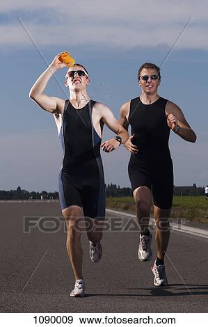 Stock Photo - A runner pouring water on his face while running in a race. Fotosearch