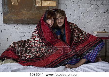 A serene couple wrapped in a blanket sitting on a bed View Large Photo Image Stock Image - A serene couple wrapped in a blanket sitting on a bed. Fotosearch