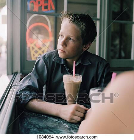 A serious teenage boy with a milkshake looking out a window View Large Photo Image Picture - A serious teenage boy with a milkshake looking out a window . Fotosearch