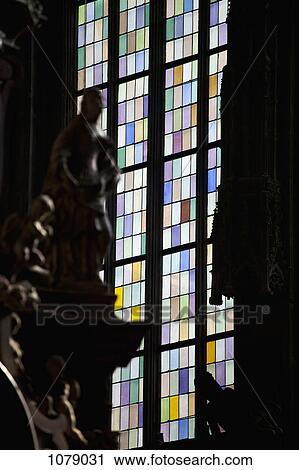 Stock Image - A stained glass window in back of craved statues, focus on window. Fotosearch