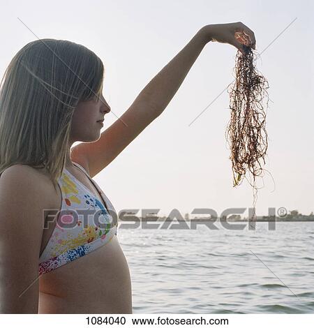 Stock Image - A teenage girl holding up seaweed. Fotosearch