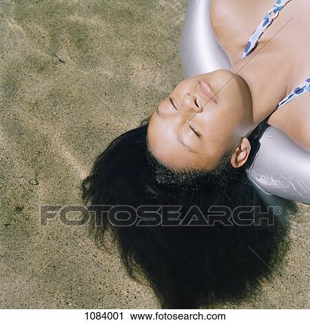 Stock Image - A teenage girl lying on an inflatable raft in shallow water. Fotosearch