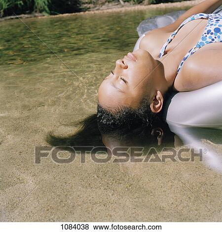 Stock Photo - A teenage girl lying on an inflatable raft in shallow water. Fotosearch