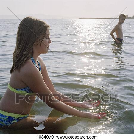 Stock Image - A teenage girl scooping on water while wading in the sea. Fotosearch