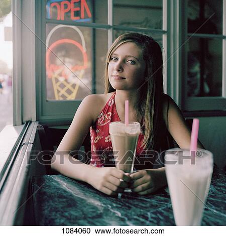 A teenage girl sitting at a table with a milkshake View Large Photo Image Stock Image - A teenage girl sitting at a table with a milkshake. Fotosearch