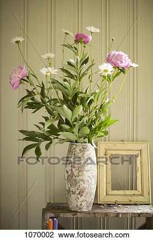 Stock Image - A vase of peonies and daisies and an empty picture frame. Fotosearch