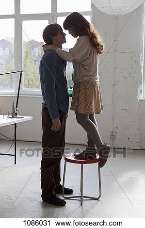 A woman standing on a stool with her arms around her tall boyfriend View Large Photo Image Stock Image - A woman standing on a stool with her arms around her tall boyfriend. Fotosearch