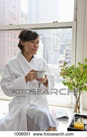 A woman wearing a bathrobe sitting on a window sill and holding a mug, looking away View Large Photo Image Stock Image - A woman wearing a bathrobe sitting on a window sill and holding a mug, looking away. Fotosearch