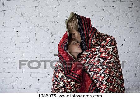 Stock Photography - A young affectionate couple wrapped in a blanket. Fotosearch