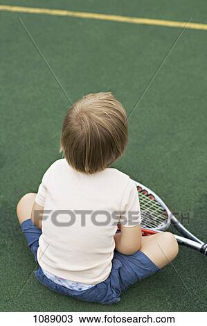 A young boy sitting on a tennis court with a tennis racket, rear view View Large Photo Image Stock Image - A young boy sitting on a tennis court with a tennis racket, rear view. Fotosearch